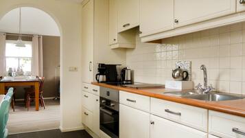 Una cocina con armarios blancos, encimera de madera, un lavabo y un comedor con mesa y sillas.