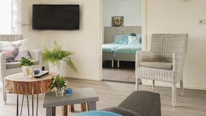 A living room with wicker furniture, a flat-screen TV, and a bed in the background.