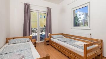 A room with two wooden beds, a window, and a view of buildings outside.