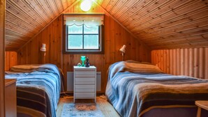 Een gezellig slaapkamer op zolder met houten wanden, een raam met gordijn, twee bedden met gestreept beddengoed, een kaptafel en een lamp.