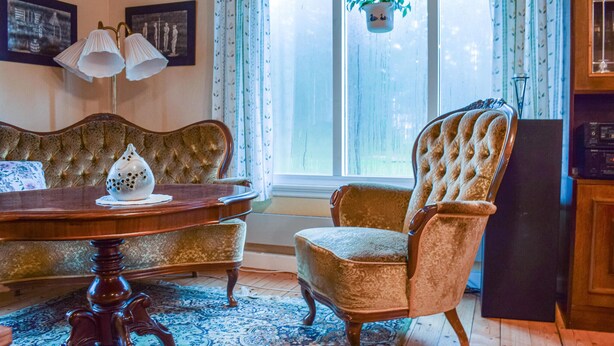 Een kamer met een antieke bank, een gestoffeerde fauteuil, een houten tafel en een kamerbreed tapijt met dessin.