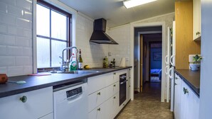 Een kleine keuken met witte kastjes, een zwarte afzuigkap, een raam en een deur naar een andere kamer.