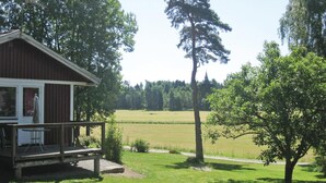 Un chalet rustique doté d’une terrasse en bois, entouré d’un champ verdoyant et d’arbres.
