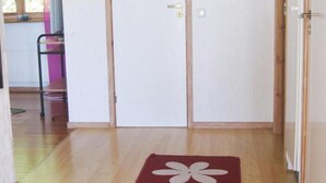 Un couloir doté d’un plancher en bois, d’une moquette rouge ornée de motifs floraux blancs et d’une porte à deux battants avec un trou de serrure.