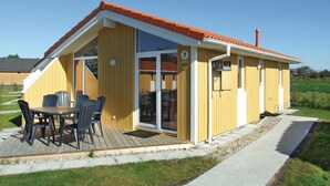 A small yellow building with a red roof, a wooden deck, and a patio table with chairs. - Friedrichskoog/deichblick 7 (Friedrichskoog)