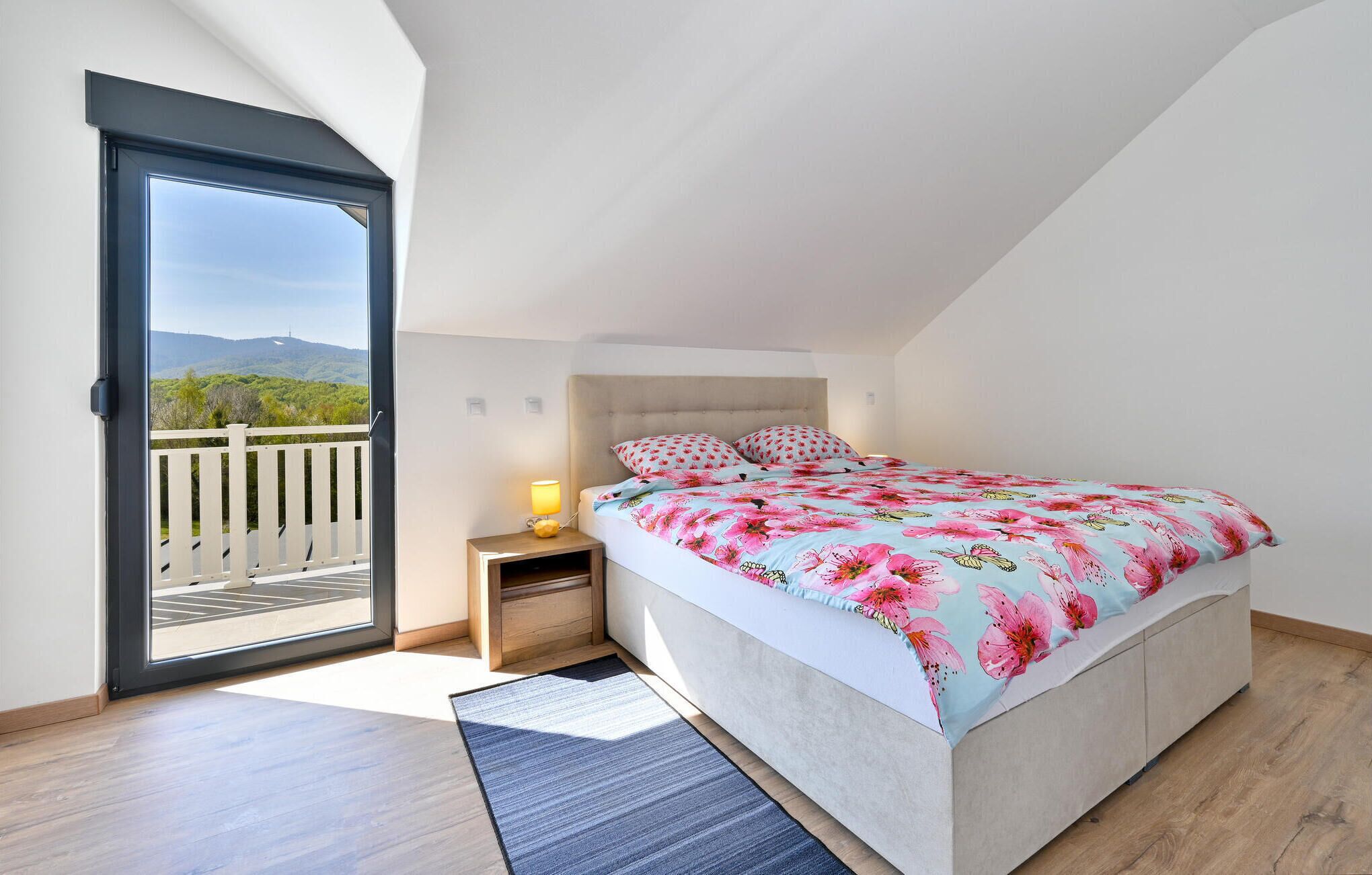 Un dormitorio con cama, mesita de noche, lámpara, vista por una puerta y balcón.