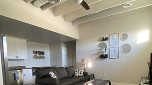A modern living room with a gray sofa, a glass coffee table, and a ceiling fan. There is a kitchen in the background with white cabinets and a refrigerator. - Quiet and cozy, a remodeled dairy with panoramic mountain views. . (Salem)