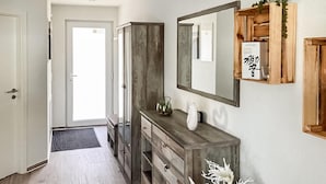 A hallway with a wooden cabinet, a mirror, and a small shelf with a book and a plant.