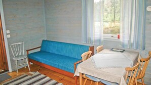 Une pièce avec un canapé bleu, une table en bois recouverte d’une nappe blanche et une fenêtre avec des rideaux.