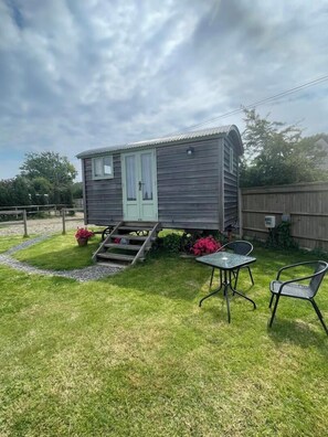 A small wooden cabin with a green door, a set of stairs leading up to it, and a patio area with two chairs and a table. - 'Get Cosy' at The Hut on a working farm by the South Coast (Hayling Island)