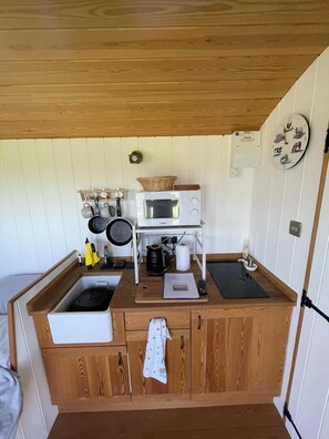 A compact kitchen with a microwave, stove, sink, and wooden cabinets. - 'Get Cosy' at The Hut on a working farm by the South Coast (Hayling Island)
