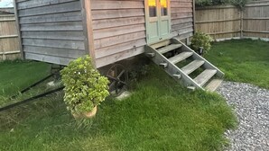 Une petite maison en bois avec un porche et un escalier menant à une porte.
