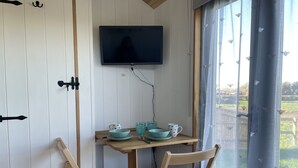 Une petite pièce avec une table en bois, deux chaises, un téléviseur fixé au mur et une fenêtre avec des rideaux.