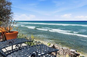 A seaside view with a clear sky, a metal table, and potted plants.