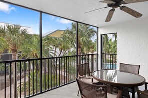A balcony with a glass table and chairs, a ceiling fan, and a view of palm trees and a swimming pool. - Charming Captiva Villa Residence, Great Amenities (Captiva)