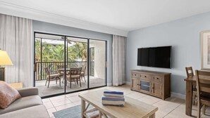 Un salon comprenant un canapé, une table basse, un téléviseur, un meuble en bois et un balcon avec une table et des chaises.
