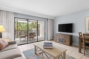 A living room with a sofa, a coffee table, a TV, a wooden cabinet, and a balcony with a table and chairs. - Charming Captiva Villa Residence, Great Amenities (Captiva)