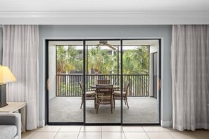 A room with a sliding glass door leading to an outdoor area with a table and chairs, a ceiling fan, and a view of palm trees. - Charming Captiva Villa Residence, Great Amenities (Captiva)