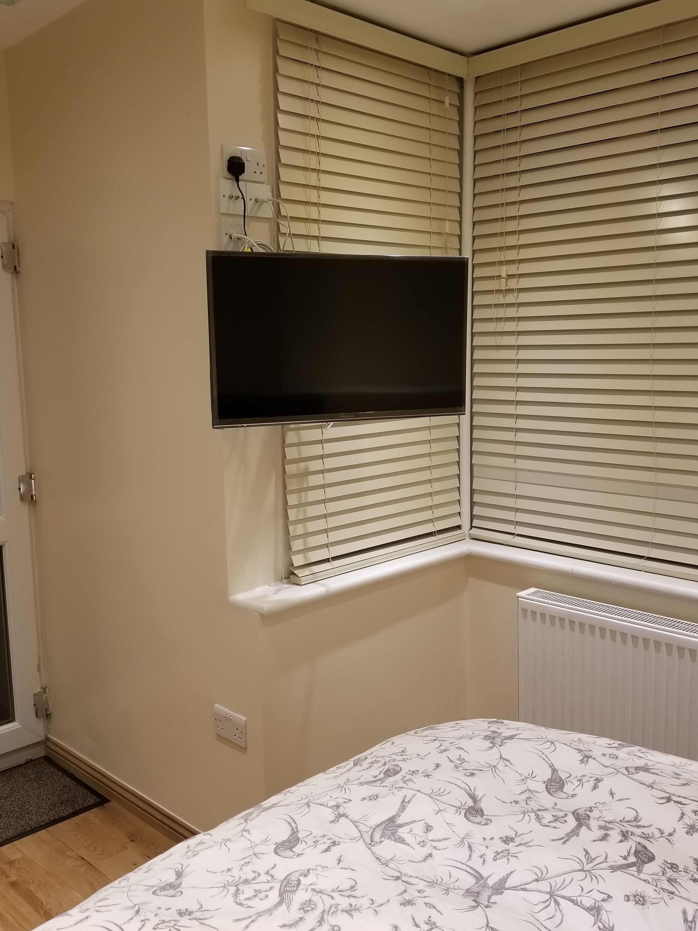 A bedroom with a bed, a mounted TV, and a window with blinds.