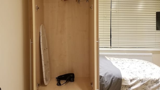 A bedroom with a wooden wardrobe, a bed with a floral bedspread, and a window with blinds. - London Luxury Apartment 1 Bed Studio 1 min walk to Redbridge Tube Station (Ilford)