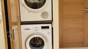 A laundry room with two stacked Bosch washing machines, a wooden cabinet above, and a wooden door to the right. - London Luxury Apartment 1 Bed Studio 1 min walk to Redbridge Tube Station (Ilford)