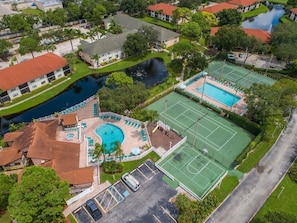 Vue aérienne d’un quartier résidentiel avec une piscine, des courts de tennis et un petit étang.