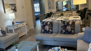 Uma sala de estar moderna com um sofá, uma mesa de centro e um espaço de jantar com uma mesa posta para quatro pessoas.