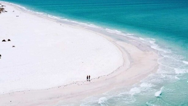 Uma praia com uma extensa faixa de areia e águas turquesa cristalinas.