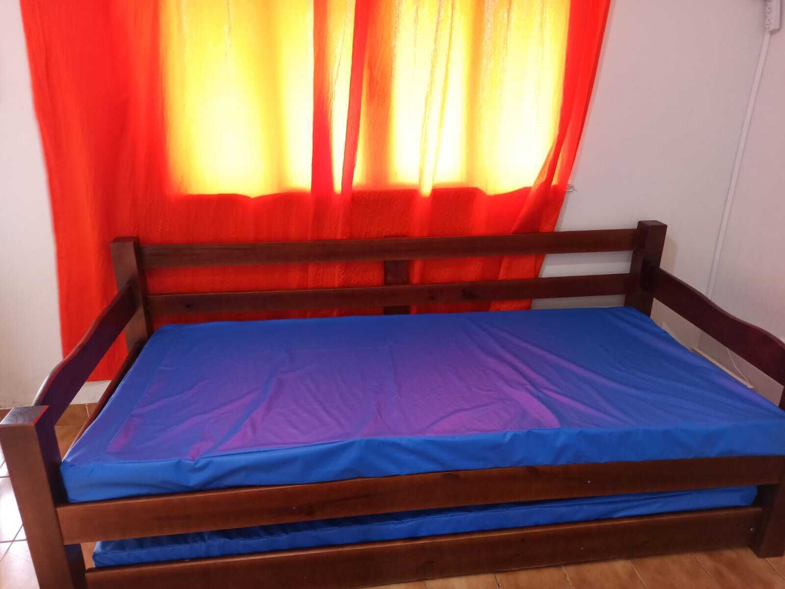 Uma cama de madeira com colchão azul e cortinas vermelhas.
