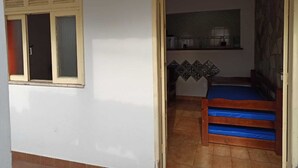 Ein kleines Zimmer mit einem Bett, einem Fenster mit Rollläden und einer Küchenzeile.
