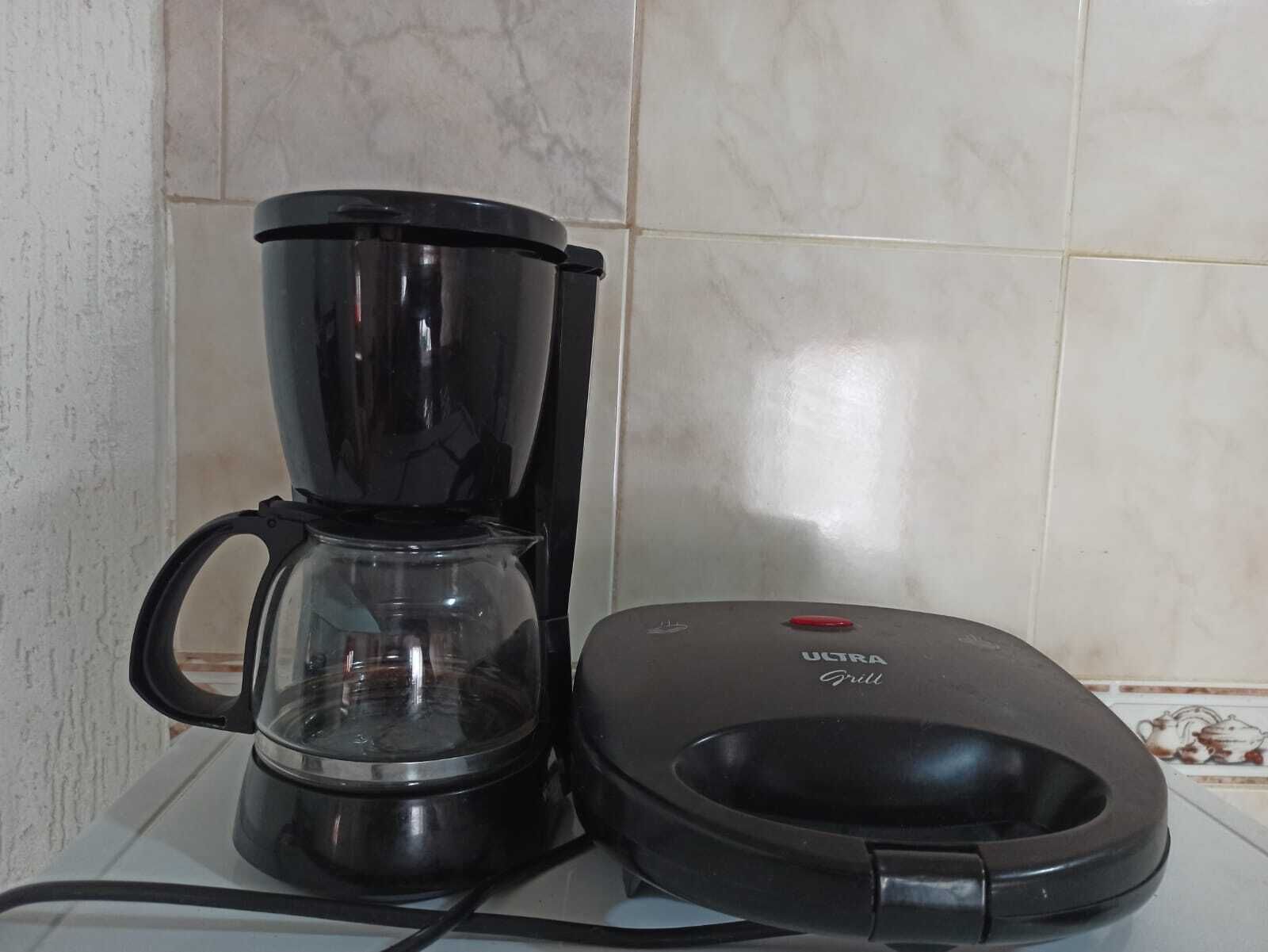 A coffee maker with a glass carafe and a black griller on a tiled countertop.