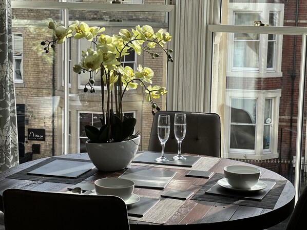 Een eettafel gedekt met een witte schaal, twee wijnglazen en een potorkidee.