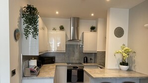 Een compacte keuken met een centraal kookeiland, een ingebouwde oven en een roestvrijstalen afzuigkap.