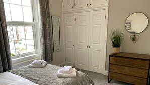 Een slaapkamer met een bed, een dressoir, een spiegel en een raam met gordijnen.