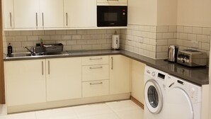 Una cucina compatta con mobili bianchi, un forno a microonde Bosch, una lavatrice e un tostapane.