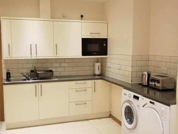 A compact kitchen with white cabinets, a Bosch microwave, a washing machine, and a toaster.