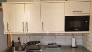Cucina con mobili bianchi, lavello in acciaio inossidabile, microonde Bosch e macchina per il caffè.