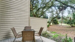 A patio with a table and chairs, a wooden deck, and a view of a wooded area. - 162 The Greens Villa Walk to Pool, Beach (Hilton Head Island)