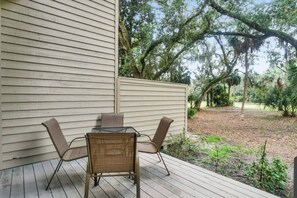 A patio with a table and chairs, a wooden deck, and a view of a wooded area.