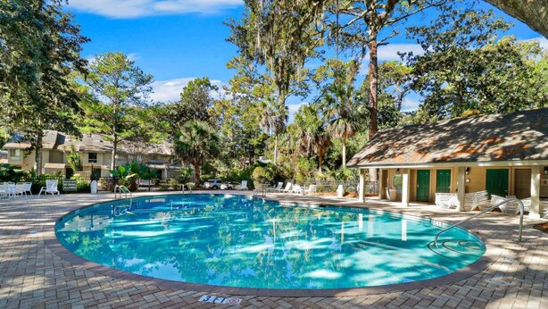 A swimming pool with a brick deck, surrounded by trees and a building with a covered area. - 162 The Greens Villa Walk to Pool, Beach (Hilton Head Island)
