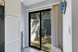 A sliding glass door leading to a backyard with a trash bin and a wooden bench.