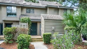 A two-story residential building with a front entrance, a small porch, and a landscaped garden with various plants and flowers. - 162 The Greens Villa Walk to Pool, Beach (Hilton Head Island)
