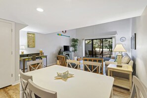 A dining area with a table, chairs, a television, and a window with a view of the outdoors.
