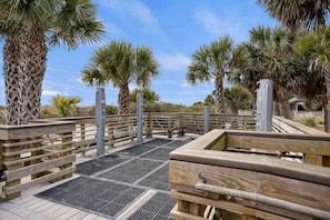 A wooden boardwalk with metal grates, surrounded by palm trees and a clear sky.