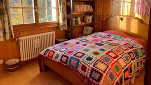 A cozy room with a wooden bed, a bookshelf, and a window with curtains.