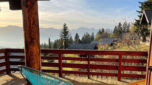 A wooden deck with two chairs, a wooden fence, and a view of mountains and trees.