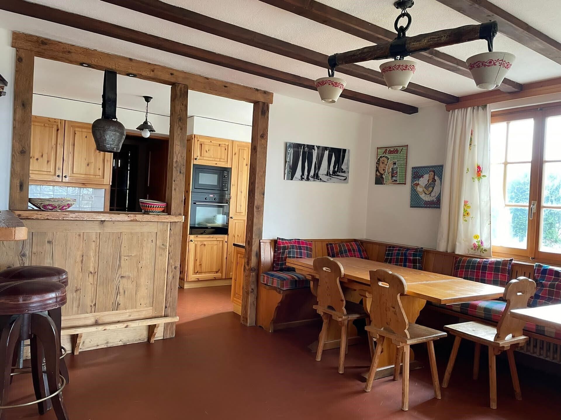 A rustic kitchen with wooden cabinets, a dining area with a bench and chairs, and a large window with curtains.