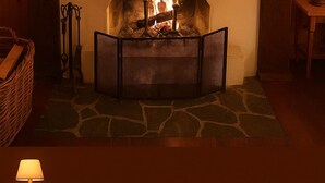 A cozy fireplace with a stone hearth, surrounded by wooden walls and a simple mantelpiece.