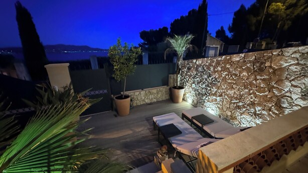 Un patio al aire libre con muro de piedra, una mesa con sillas y plantas en macetas.