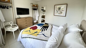 Un dormitorio con cama, televisor, armario, silla y espejo.
